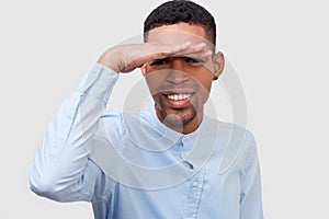 Closeup portrait of smiling African American man posing for advertisement wearing blue shirt, looking away with hand on forehead