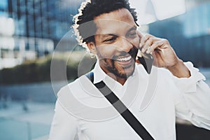 Closeup portrait of smiling American African man using smartphone to call friends at sunny street.Concept of happy young