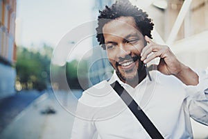 Closeup portrait of smiling American African man using smartphone to call friends at sunny street.Concept of happy young