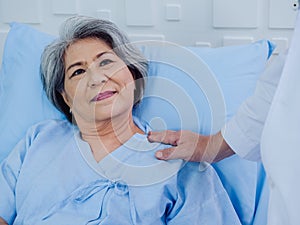 Closeup portrait of smiling Asian elderly, senior woman patient in light blue dress lying on bed.