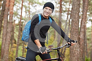 Closeup portrait of smiling cyclist man riding mountain bike on trail in park or forest, enjoing fresh air and beautiful nature,