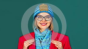 Closeup portrait of smiling fashionable girl in red jacket, knitted hat and blue scarf. Autumn-winter fashion for women