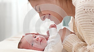 Closeup portrait of smiling loving mother stroking and looking on her newborn baby son lying on bed on bright sunny day