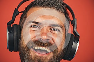 Closeup portrait of smiling man listening music with headphones. Handsome bearded hipster in wireless headphones