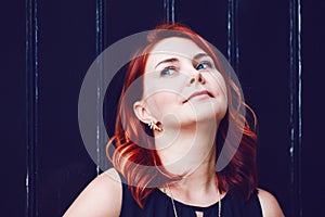 Closeup portrait of smiling middle aged white caucasian woman with waved curly red hair in black dress looking away