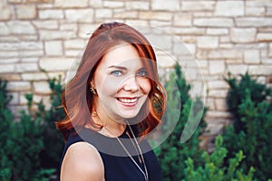 Closeup portrait of smiling middle aged white caucasian woman with waved curly red hair in black dress looking in camera