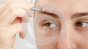 Closeup portrait of smiling young woman forming eyebrows with tweezers after having bath. Concept of beautiful female, makeup at