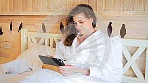 Closeup portrait of smiling young woman lying in bed and working on tablet computer