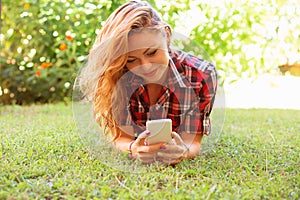 Woman texting by phone and lying on meadow