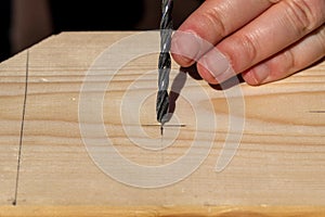 A closeup portrait of someone aiming and placing the tip of a wood drill bit at the drawn pencil marking made on a wooden plank to