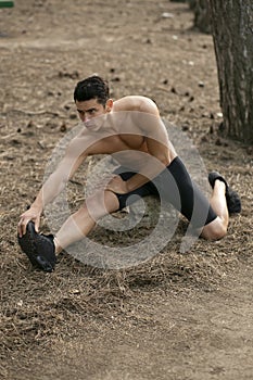 Closeup portrait of a sportsman doing stretching exercises in the park. Healthy lifestyle concept