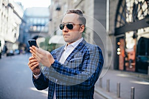 Closeup Portrait of stylish handsome young man standing outdoors. Man wearing jacket and shirt. man using mobile phone