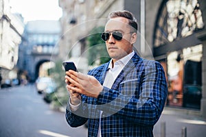 Closeup Portrait of stylish handsome young man standing outdoors. Man wearing jacket and shirt. man using mobile phone