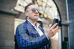 Closeup Portrait of stylish handsome young man standing outdoors. Man wearing jacket and shirt. man using mobile phone