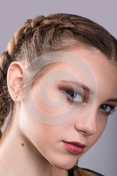 Closeup portrait of a teenage girl with braided pigtails standing in front of a and gray background