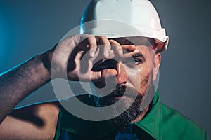 Closeup portrait of tired builder in construction helmet. Fatigued worker wipes sweat from forehead. Hard work at