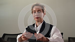 Closeup portrait of tired gray-haired middle-aged business woman using mobile phone indoors, feeling discomfort from dry