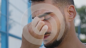 Closeup portrait of tired upset sad young Middle Eastern Arab man rubbing bridge of nose. Millennial Indian guy student