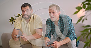 Closeup portrait of two adult caucasian men playing video games together sitting on couch at home indoors. Happy man