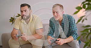 Closeup portrait of two adult caucasian men playing video games together sitting on couch at home indoors. Man winning