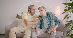 Closeup portrait of two caucasian men watching football on TV emotionally together sitting on couch at home indoors