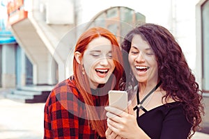 Closeup portrait two surprised girls looking at phone discussing latest gossip news Young shocked funny women friends reading