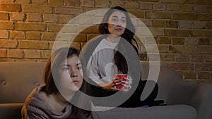 Closeup portrait of two young female friends watching TV while resting in a cozy apartment indoors