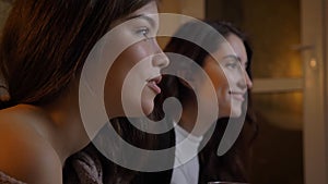 Closeup portrait of two young pretty women watching TV laughing happily in a cozy apartment indoors