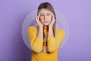 Closeup portrait of unhappy woman with serious facial expression, looking directly at camera, keeping fingers on her temples,