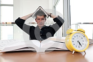 Closeup portrait of white man surrounded by tons of books, alarm clock, stressed from project deadline, study, exams