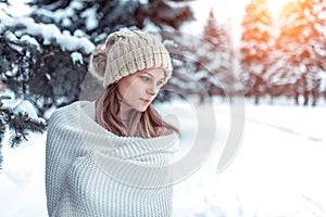 Closeup portrait winter woman background snow and Christmas trees. White warm winter hat, large long woolen plaid