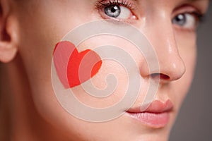 Closeup portrait of woman face with red heart on her skin