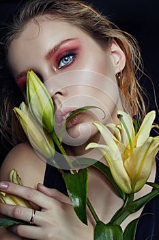 Closeup portrait of woman with flowers lilies in his hands, bright contrasting makeup on the girl`s face. Wet hair and clean