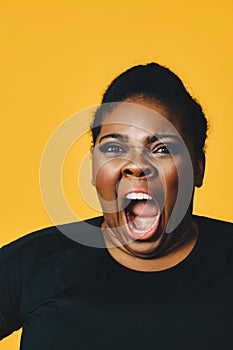 closeup portrait of a young adult african american woman in shock with mouth open screaming on yellow background