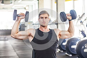 Closeup portrait of young adult man muscular built handsome athlete working out in a gym, sitting and holding two dumbbell with