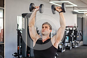 Closeup portrait of young adult man muscular built handsome athlete working out in a gym, sitting and holding two dumbbell with