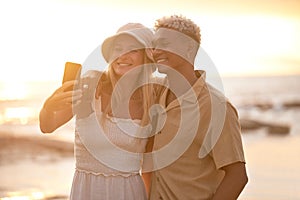 Closeup portrait of an young affectionate mixed race couple standing on the beach and smiling and taking a selfie with a