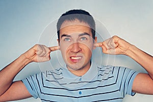 Closeup portrait young, angry, unhappy, stressed man covering his ears, looking up, to say, stop making loud noise it`s giving