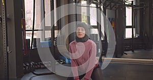 Closeup portrait of young attractive athletic muslim female making squats with dumbbell in gym indoors