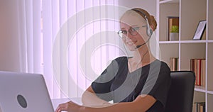 Closeup portrait of young attractive caucasian businesswoman in glasses and headphones using laptop looking at camera