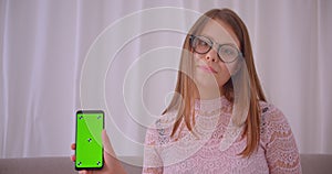 Closeup portrait of young attractive caucasian female in glasses using phone and showing green chroma screen to camera