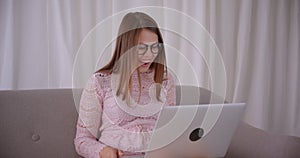 Closeup portrait of young attractive caucasian female having a video call on laptop laughing happily sitting on couch