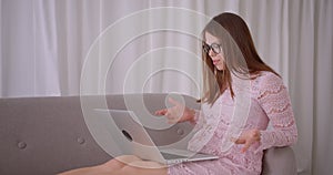 Closeup portrait of young attractive caucasian female having a video call on laptop sitting on couch laidback indoors