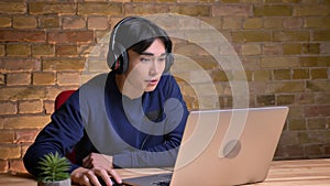 Closeup portrait of young attractive korean man using laptop and putting his headphones on