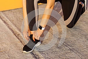 Closeup portrait of young attractive sporty woman wearing black sporwear in morning on street standing on knee and preparing for