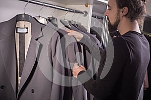 Closeup portrait of a young bearded guy, millennial, in a men`s clothing store chooses a business suit for work