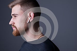 Closeup portrait of a young bearded guy of twenty-five years old, standing in profile. In wireless white headphones. Sporty style