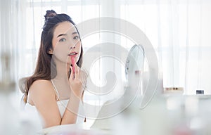 Closeup portrait of young beautiful asian girl put lipstick on with mirror for makeup routine.