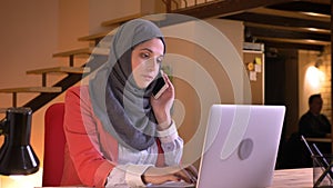 Closeup portrait of young beautiful muslim businesswoman in hijab having a casual conversation on the phone sitting in