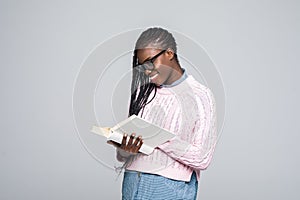 Portrait of a young beautiful woman is reading a book with glasses isolated over gray background